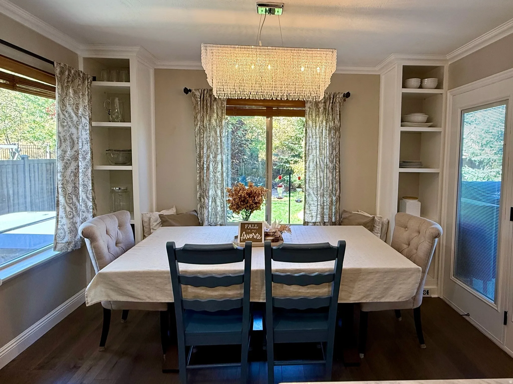 Dining space featuring wood-finish flooring, a contemporary crystal chandelier, and a large window providing natural light