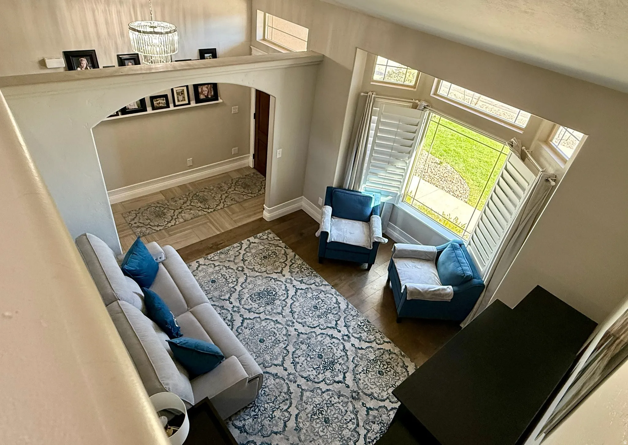 Two-story living area with high ceilings, large bay windows, wood-finish flooring, and an arched entryway