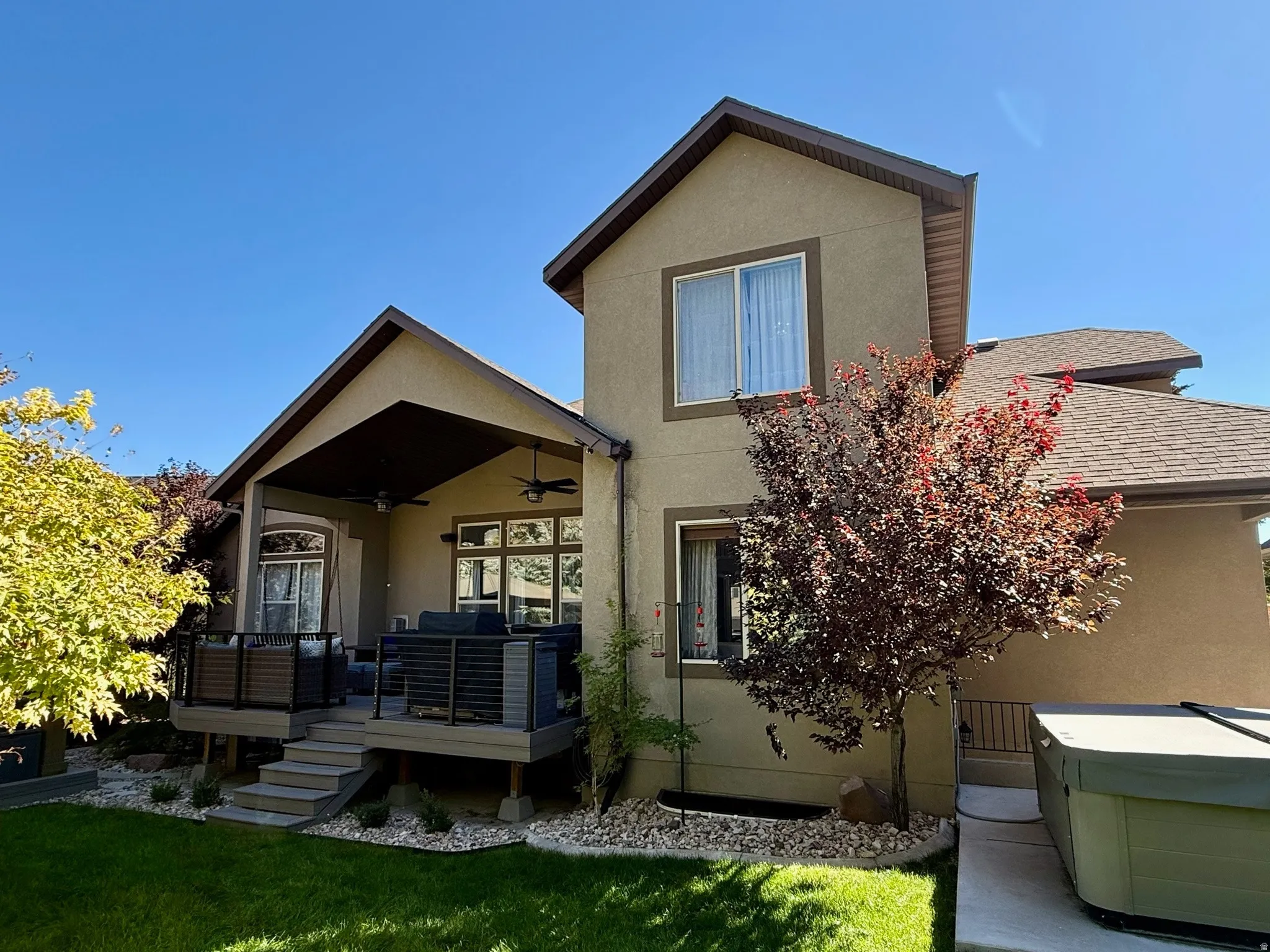 Rear exterior featuring a covered deck with integrated ceiling fans, a lower patio, and a hot tub