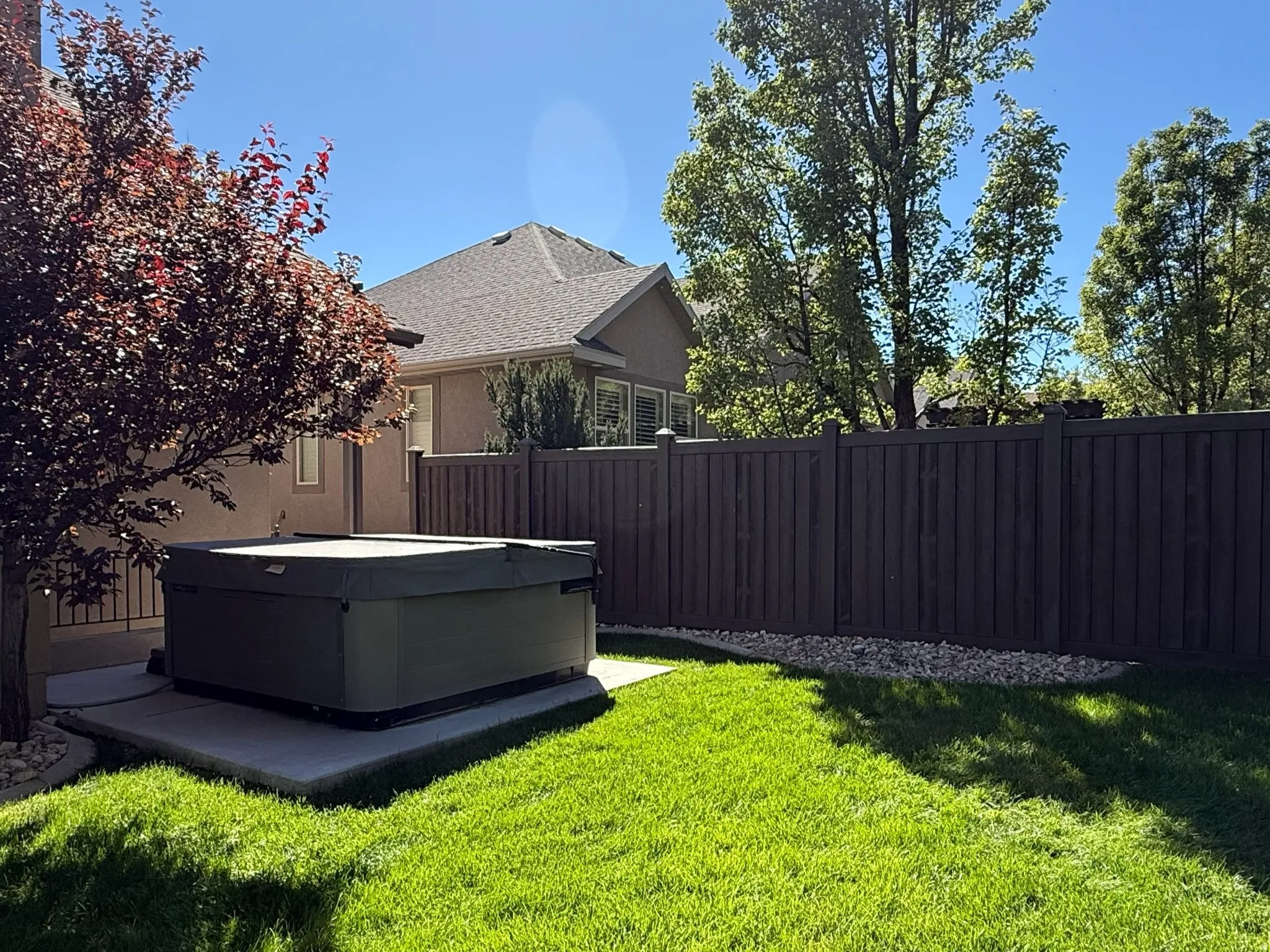 Private backyard featuring a hot tub on a concrete pad, surrounded by lush green lawn