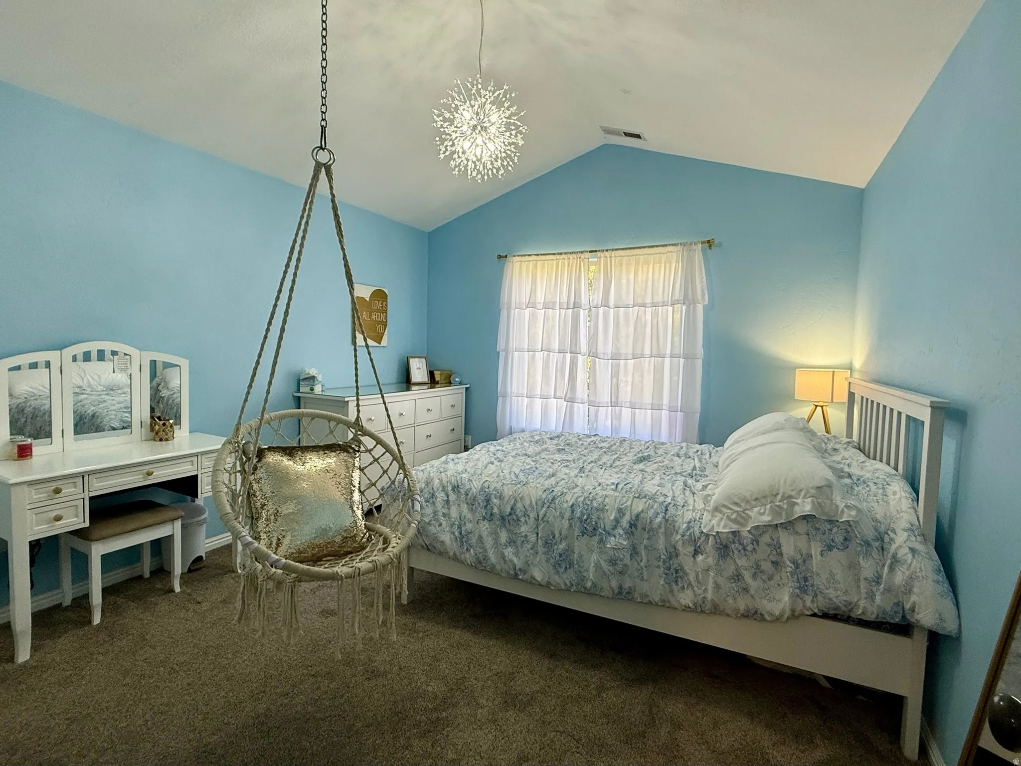 Vaulted ceiling room featuring a contemporary hanging chair, large window with privacy sheers, and plush carpet flooring