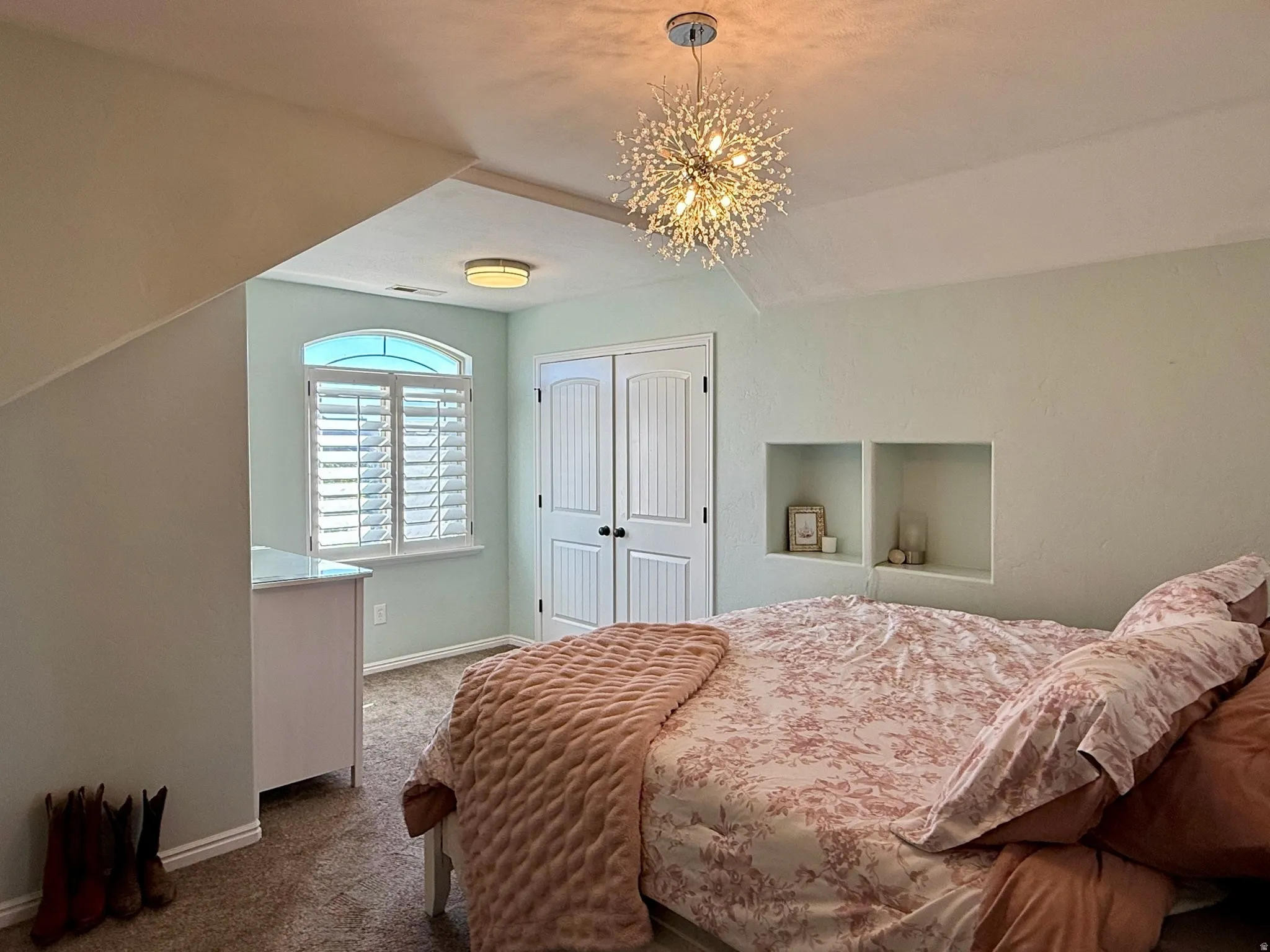 Bedroom featuring an arched window with plantation shutters, built-in wall niches, and a contemporary sputnik-style ceiling fixture