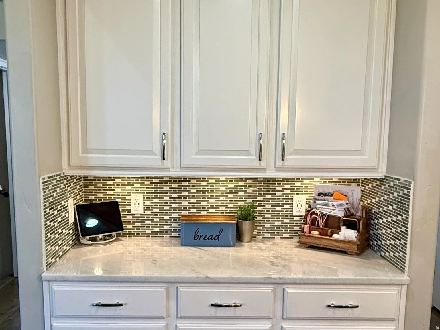White cabinetry featuring both upper and lower storage, a patterned tile backsplash, and a light-toned countertop