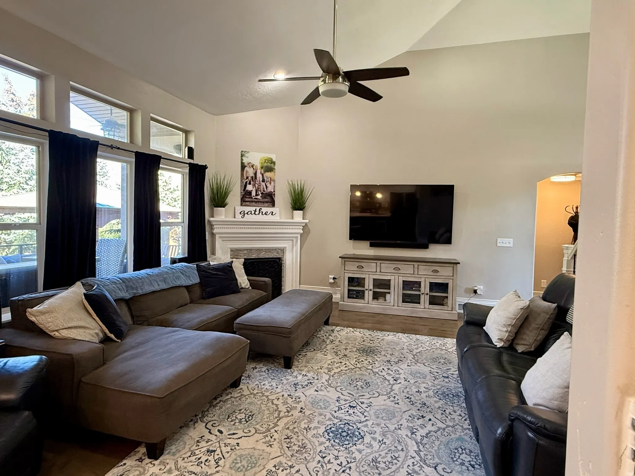 Vaulted ceilings with a ceiling fan, a fireplace with a white mantel, and multiple windows with transoms