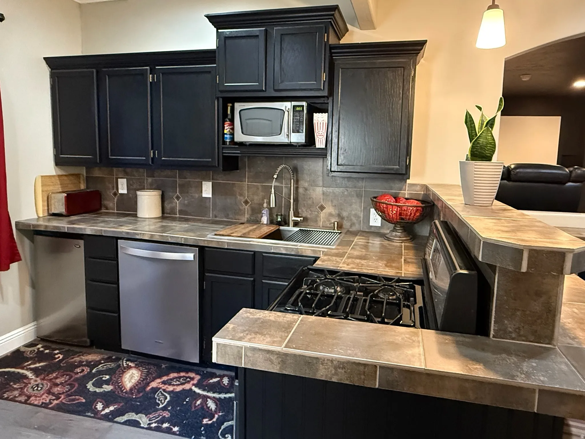 Kitchen featuring dark wood cabinetry, stainless steel appliances, a gas range, and tile countertops with a coordinating backsplash