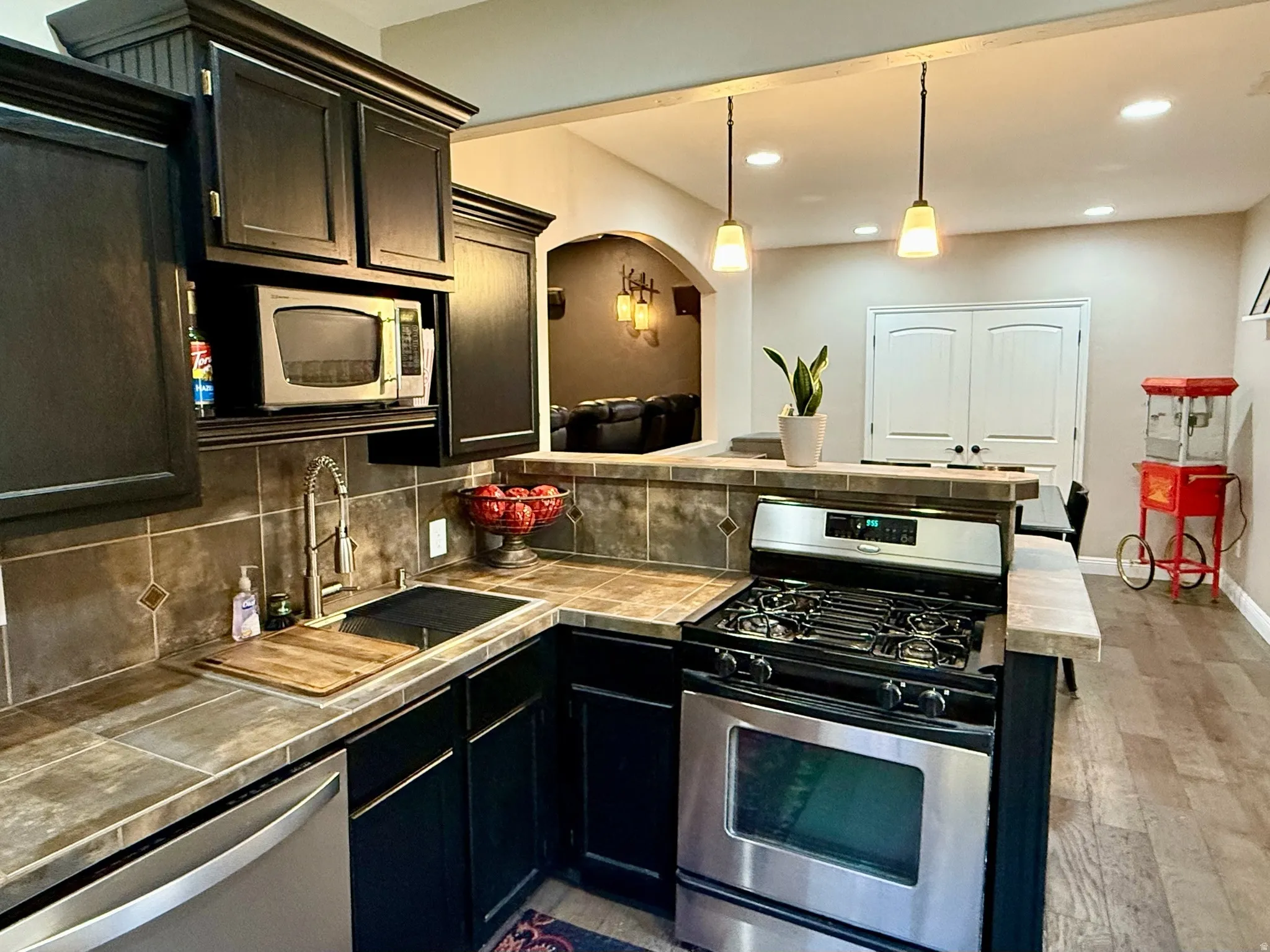 Basement Kitchen featuring dark wood cabinetry, tile countertops, and stainless steel appliances including a gas range and built-in microwave