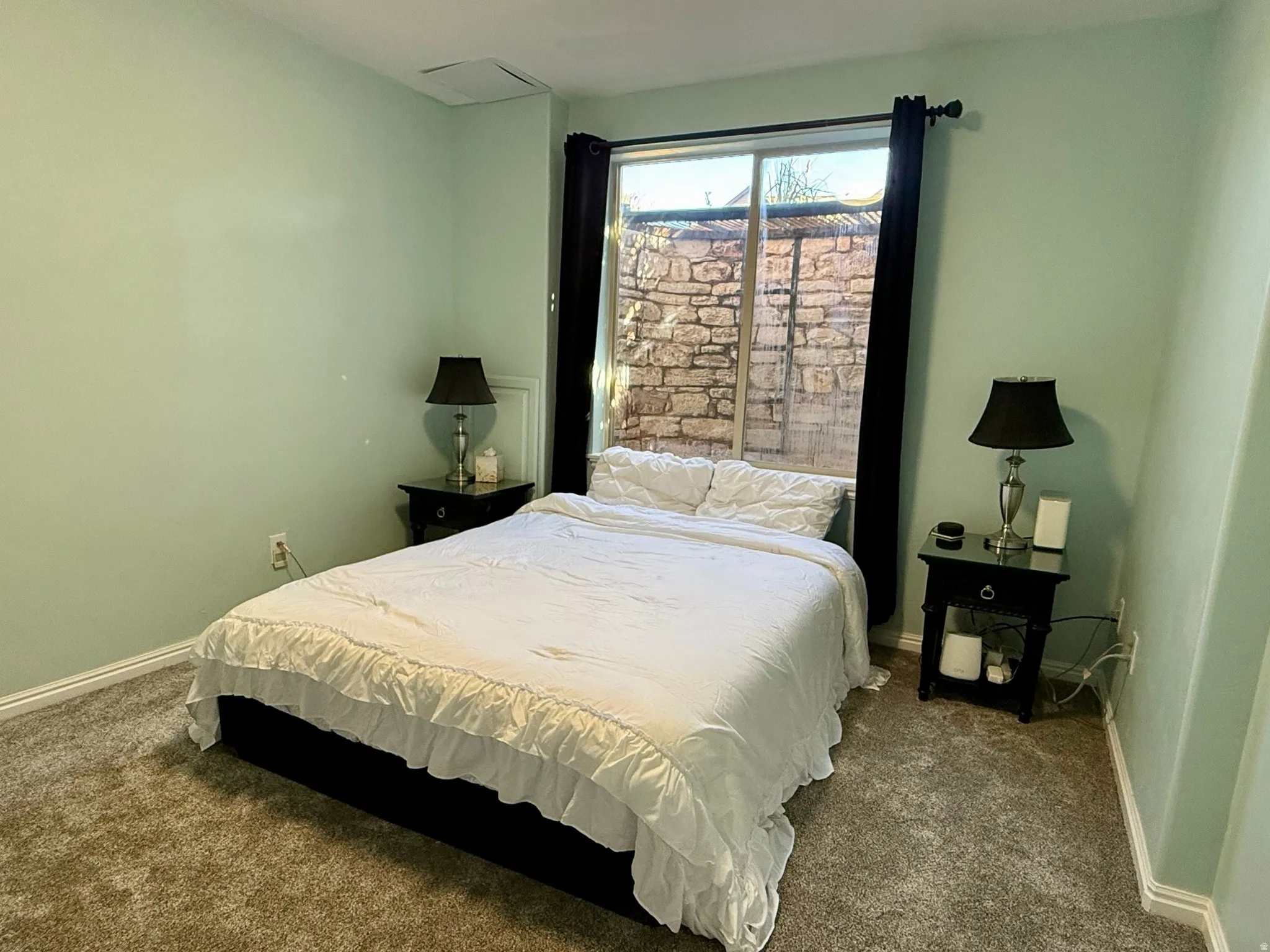 Room featuring light green painted walls, a window with dark curtains, and plush neutral-toned carpeting