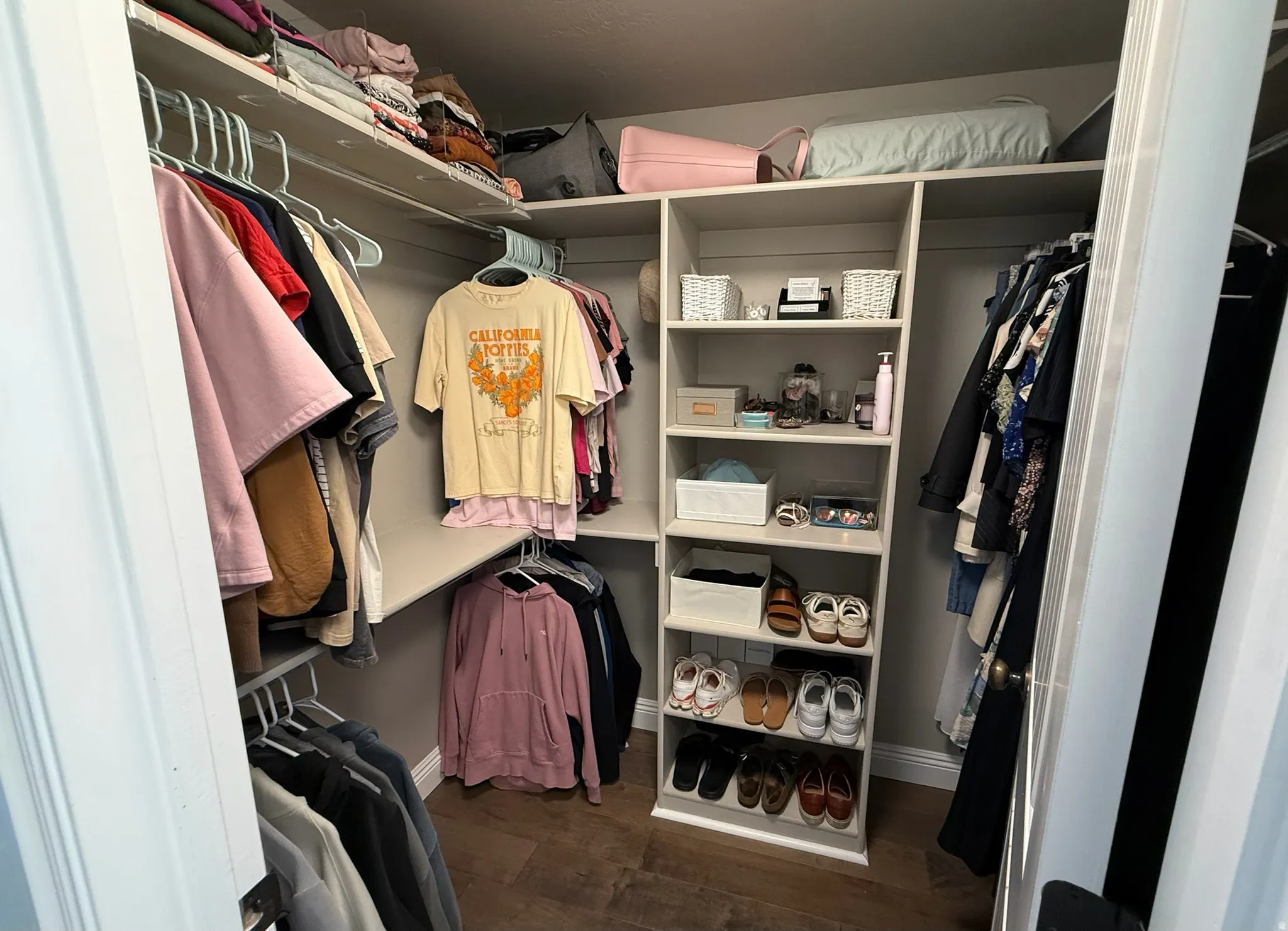 Master Walk-in closet featuring integrated shelving, multiple hanging rods, corner shelving unit, and wood-finish flooring
