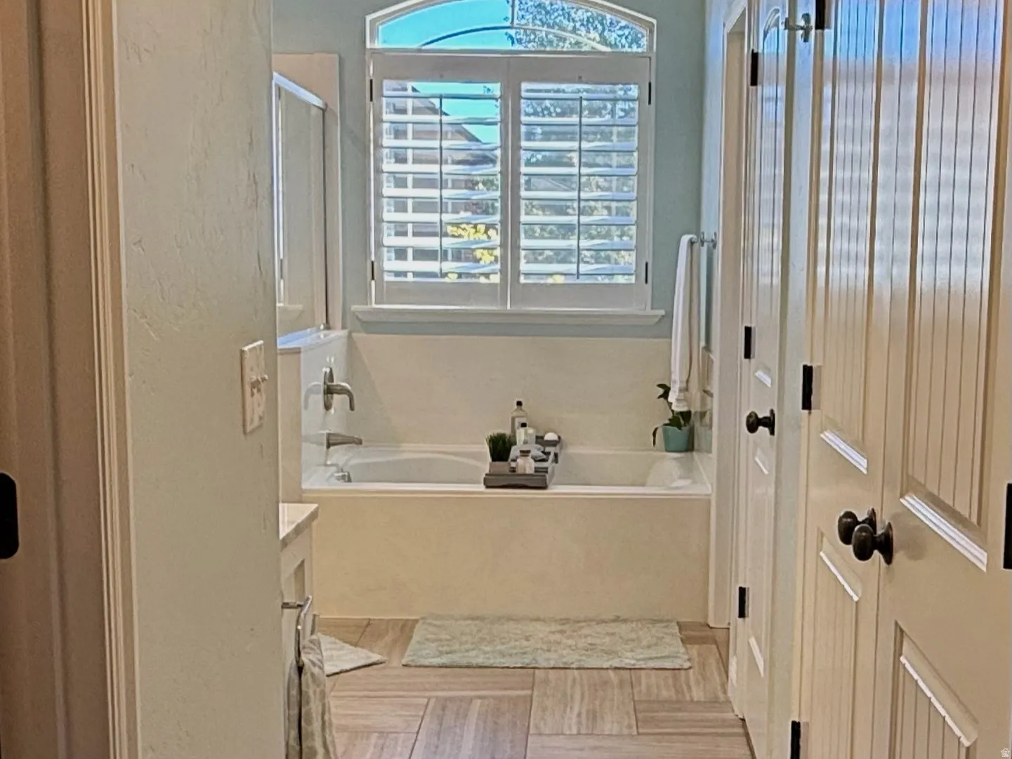 Bathroom featuring a built-in soaking tub under an arched window with plantation shutters