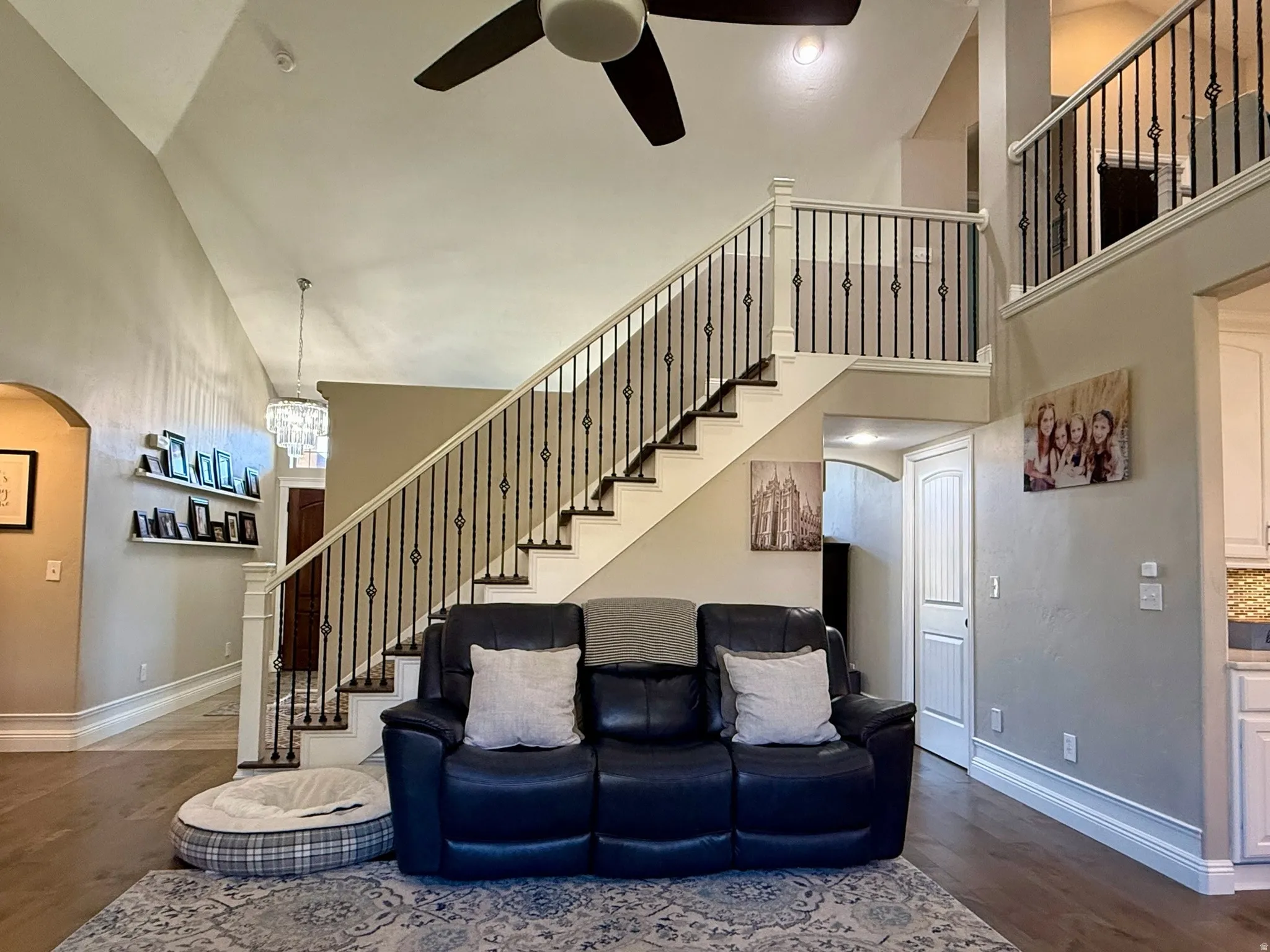 Vaulted ceilings enhance this living space featuring a dual-level staircase with wrought iron balusters, wood-finish flooring, and a ceiling fan