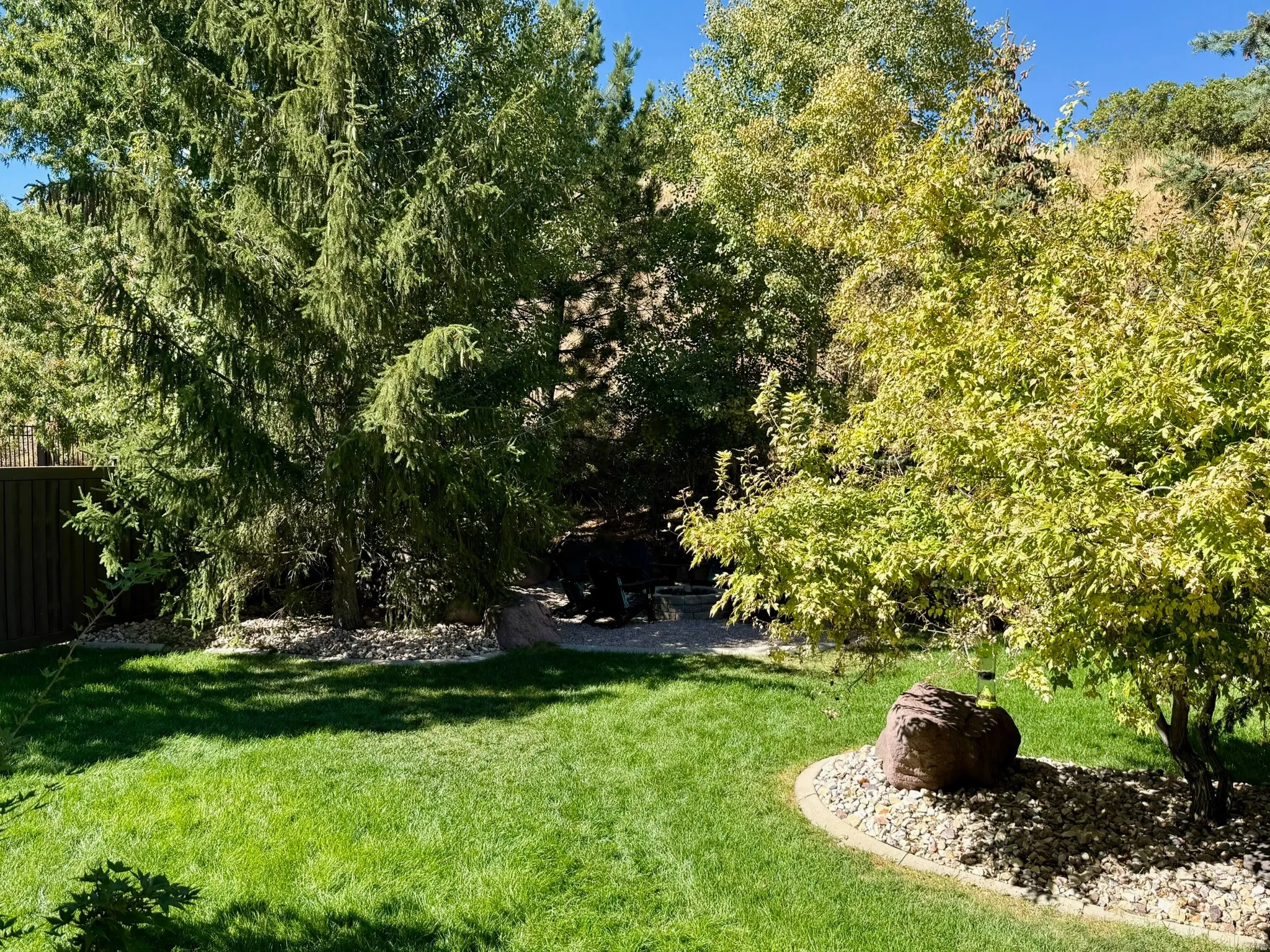 Expansive landscaped backyard featuring a manicured lawn, mature trees, and decorative rock beds