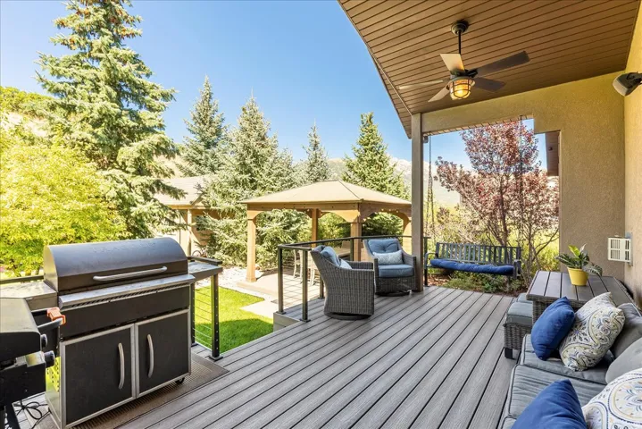 Expansive outdoor deck featuring wood-finish flooring, a covered patio area with a ceiling fan, and a built-in gazebo structure