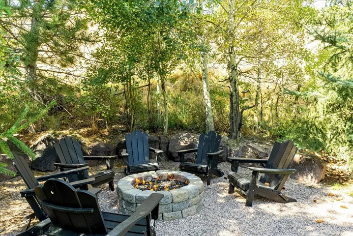 Outdoor fire pit area with stone block construction, surrounded by natural landscaping, and mature trees