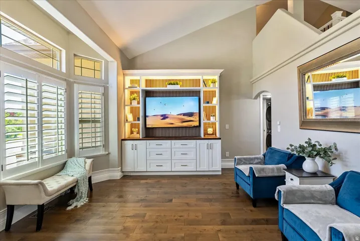 Vaulted ceiling with recessed lighting, wood-finish flooring, custom built-in media center with integrated lighting, plantation shutters, and an arched doorway