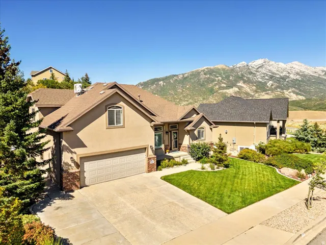 Stucco exterior with stone accents, attached two-car garage, concrete driveway, front yard landscaping, and mountain scenery