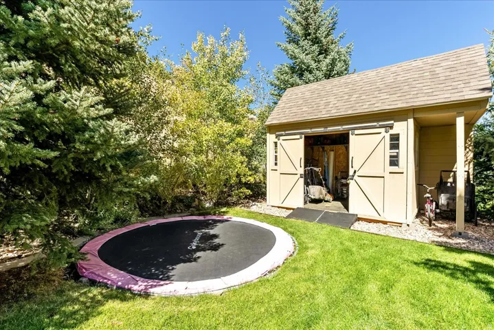 Manicured lawn with mature landscaping and a freestanding shed featuring a gabled roof and sliding barn doors