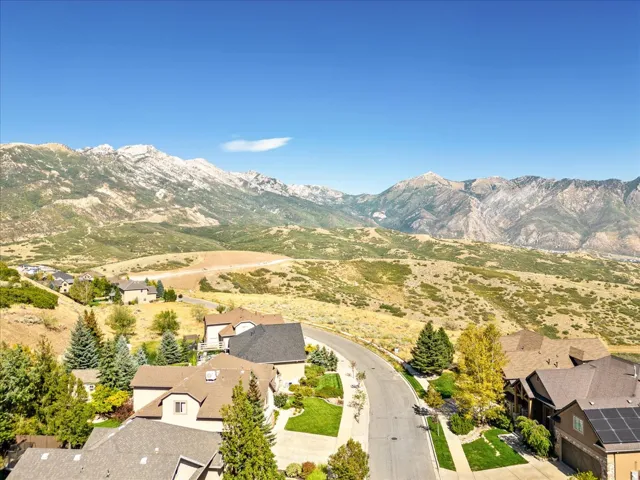Mountainous backdrop, residential street, sloped terrain, scattered trees, clear sky