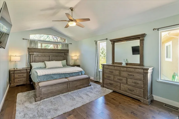 Primary Suite- Vaulted ceiling, ceiling fan with integrated lighting, wood-finish flooring, multiple windows, and light-colored walls