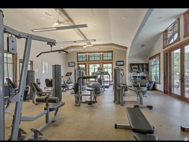 Spacious fitness center featuring a variety of exercise equipment, high vaulted ceilings with exposed beams, and large windows with integrated French doors