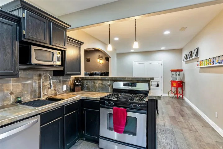 Kitchen featuring dark wood-finish cabinetry, stainless steel appliances, tiled countertops, and a tiled backsplash