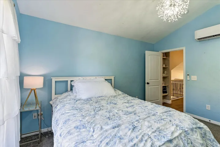 Vaulted ceiling featuring a decorative light fixture, carpeted flooring, and a wall-mounted air conditioning unit