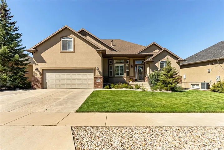Stucco exterior with brick accents, attached two-car garage, manicured lawn, and mature landscaping