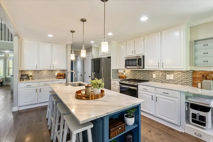 Kitchen featuring wood-finish flooring, white cabinetry, a tiled backsplash, stainless steel appliances, and an island with a light-colored countertop