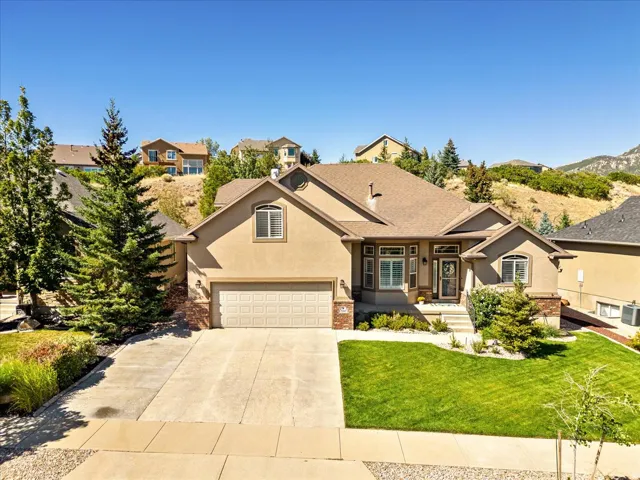 Stucco exterior with brick accents, attached two-car garage, concrete driveway, front lawn, and mature landscaping