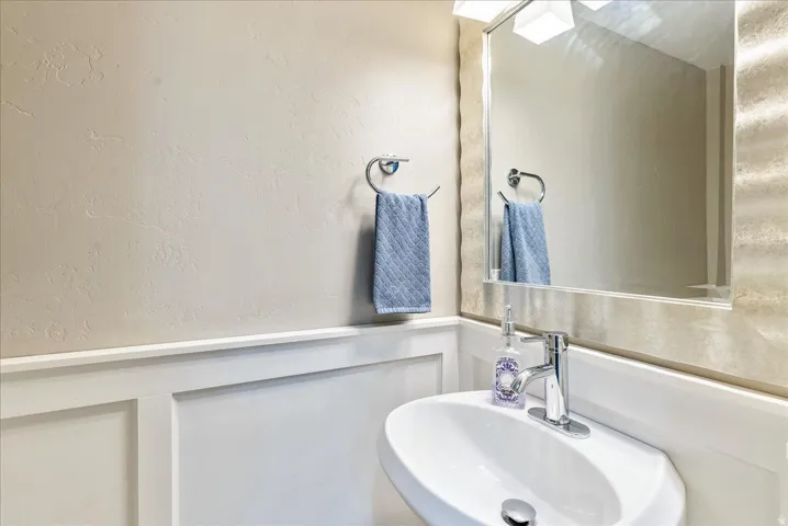 Half Bath-Wainscoting paneling with a modern wall-mounted sink, chrome faucet, and a large mirror with a textured frame