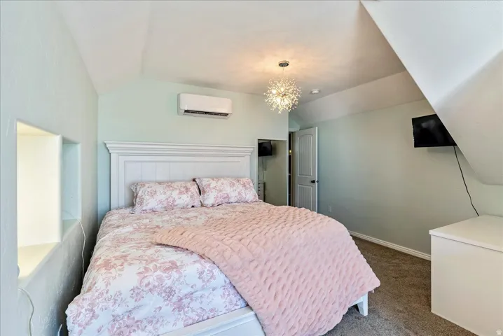 Recessed wall shelving, wall-mounted climate control unit, overhead chandelier, white paneled door, and sloped ceiling