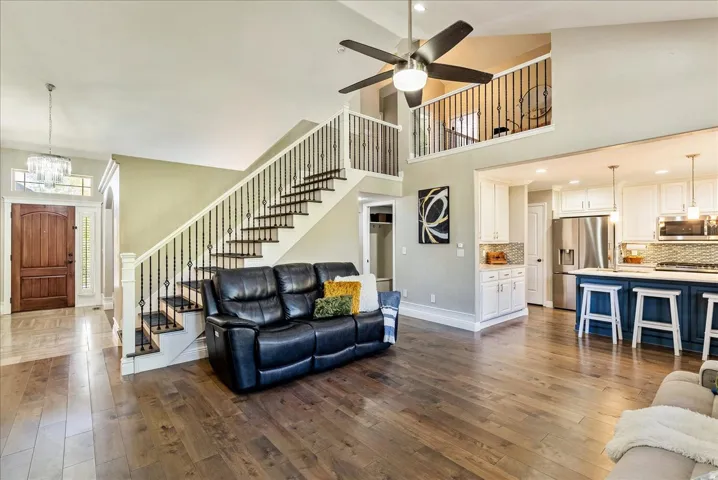 Open-concept living area with wood-finish flooring, a two-story ceiling, and a prominent staircase with wrought iron balusters
