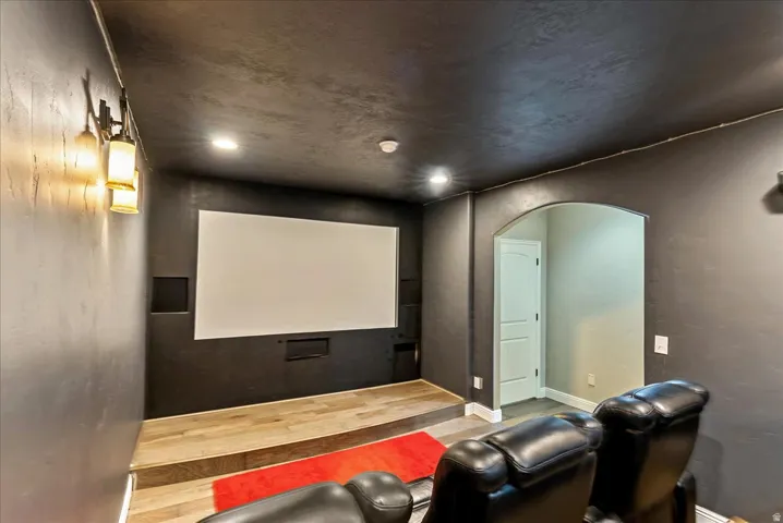 Integrated projection screen with built-in speakers, raised wood-finish platform, recessed lighting, and an arched doorway
