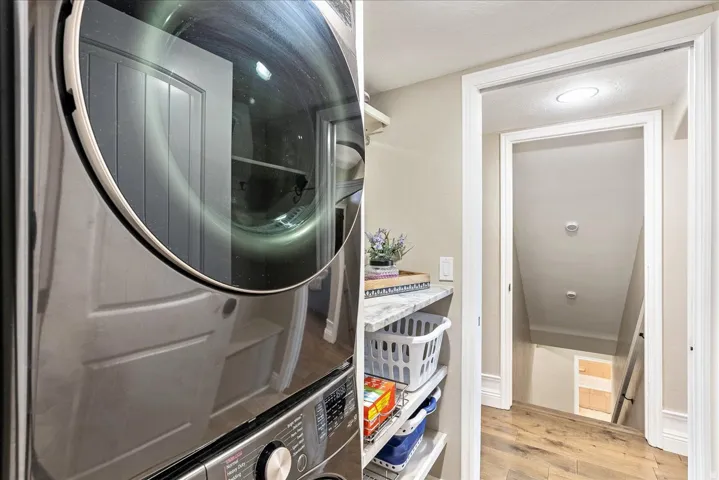 Laundry area featuring a stacked washer and dryer, built-in shelving, and a granite-finish countertop