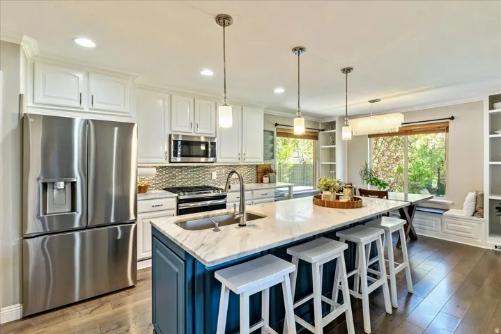 Kitchen featuring a large island with stone countertop, stainless steel appliances, wood-finish flooring, and built-in shelving