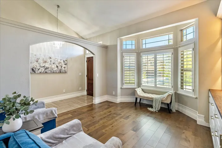 Hardwood flooring, arched doorway, vaulted ceiling, bay window, and plantation shutters