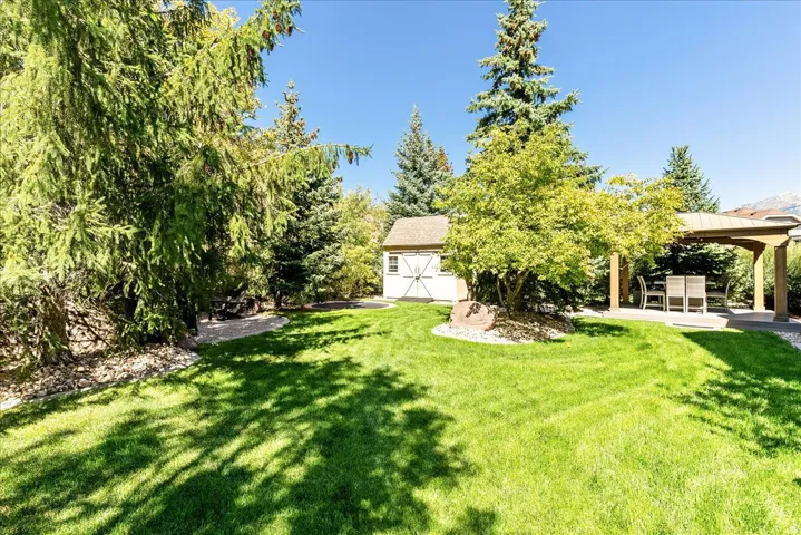 Expansive lawn with mature trees, a detached storage shed, and a covered outdoor patio area