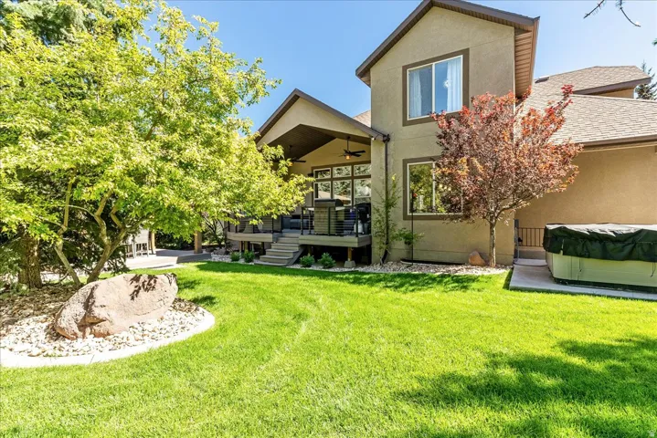 Expansive green lawn, elevated covered patio with integrated lighting, multiple mature trees, and a ground-level concrete patio
