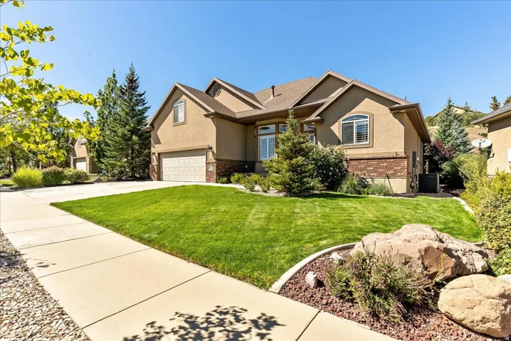 Stucco exterior with brick detailing, attached two-car garage, mature landscaping, and a concrete driveway