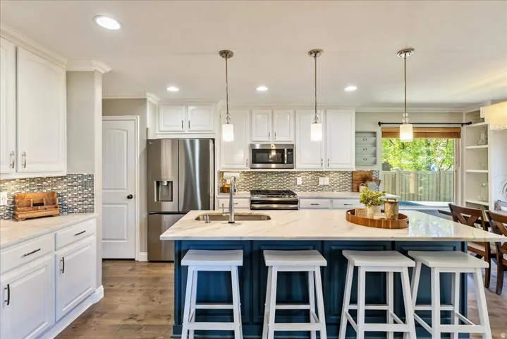 Kitchen featuring white upper and lower cabinetry, a blue island with seating, stainless steel appliances, and wood-finish flooring