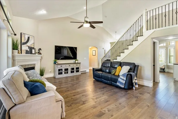 Vaulted ceilings, wood-finish flooring, fireplace with mantel, open staircase with wrought iron balusters, and a ceiling fan