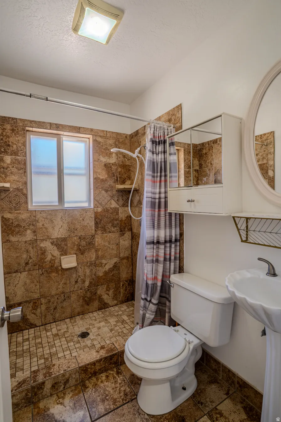 Tiled shower with mosaic floor, pedestal sink, and wall-mounted storage cabinet