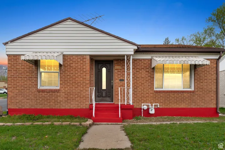 Brick facade with white siding gable, contrasting red foundation, and a central entry featuring a dark-paneled door