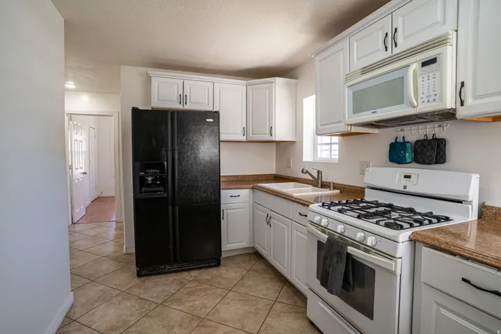 White cabinetry with dark hardware, stone-finish countertops, and a double basin sink