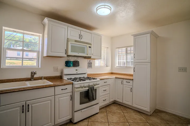 Kitchen featuring white shaker-style cabinetry, a white gas range with an above-range microwave, a double basin sink, and tile flooring