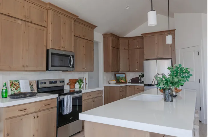 Spacious kitchen featuring natural wood cabinetry, light-toned countertops, a full suite of stainless steel appliances, a tile backsplash, and an integrated kitchen island sink