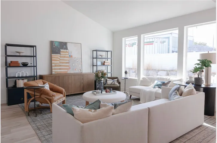 Spacious living area featuring abundant natural light from multiple large windows, wood-finish flooring, and a vaulted ceiling