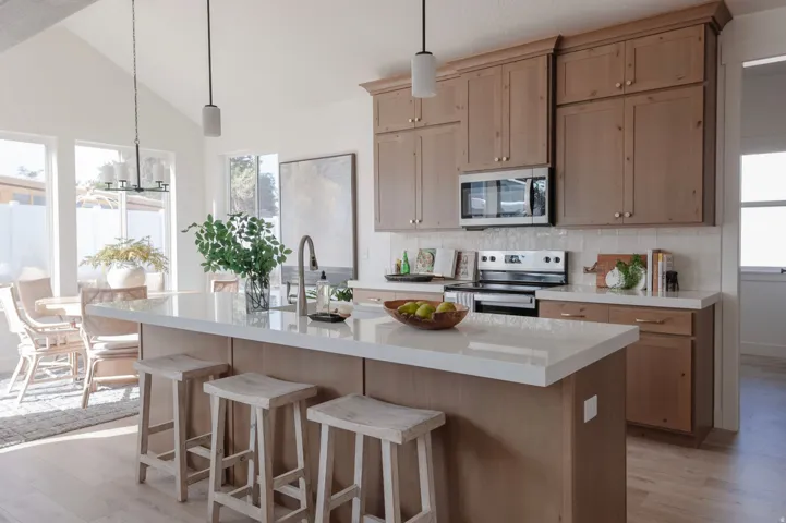 Kitchen featuring a central island with a solid surface countertop, light wood-finish cabinetry, stainless steel appliances, a tile backsplash, and light wood-finish flooring