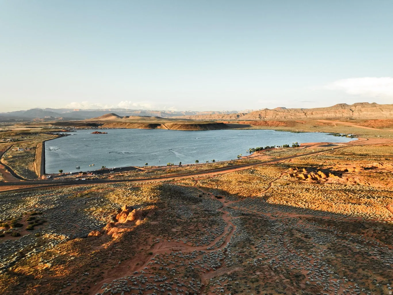Expansive desert landscape featuring a large body of water, distant mountain ranges, and rugged terrain