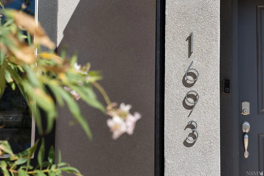 Contemporary exterior featuring stucco siding, vertical house numbers, and a dark entry door with modern hardware