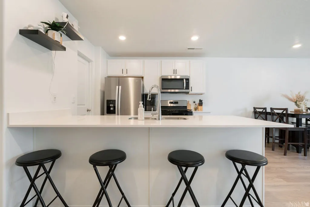 Modern kitchen featuring white cabinetry, stainless steel appliances, a breakfast bar, recessed lighting, and light wood-finish flooring